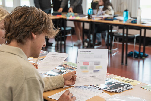 Kollegiat bei Workshop über Schulter fotografiert, hält Blatt „Meine Interessen“