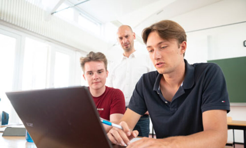 Ein junger Dozent erklärt zwei Jungen inhalte des Abiturs. 