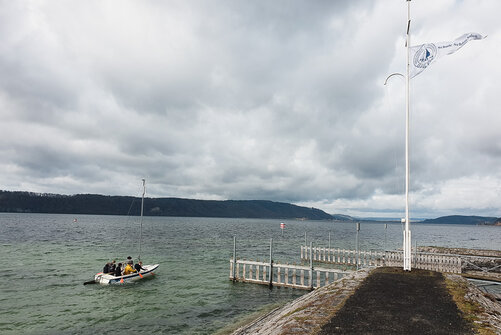 Spetzgarter Hafen mit Block über den Bodensee bei bewölktem Wetter. Links ist ein Segelboot auf dem See und rechts weht eine Fahne der Schule Schloss Salem im Wind.