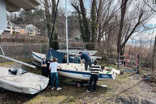 Kollegiat:innen putzen ein Segelboot, welches noch an Land steht. 
