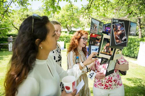 Gäste betrachten Collagen der Kollegiat:innen im Garten des Schloss Salems. 