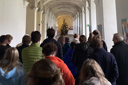 Kollegiat:innen von hinten in langem Gang mit Weihnachtsbaum am Ende.