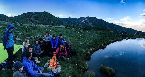 Kollegiaten sitzen auf der Outdoor Exkursion um ein Lagerfeuer am See