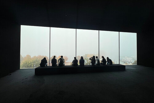 Silhouette von Kollegiat:innen auf Bank vor Fenster im Vorarlberg Museum.