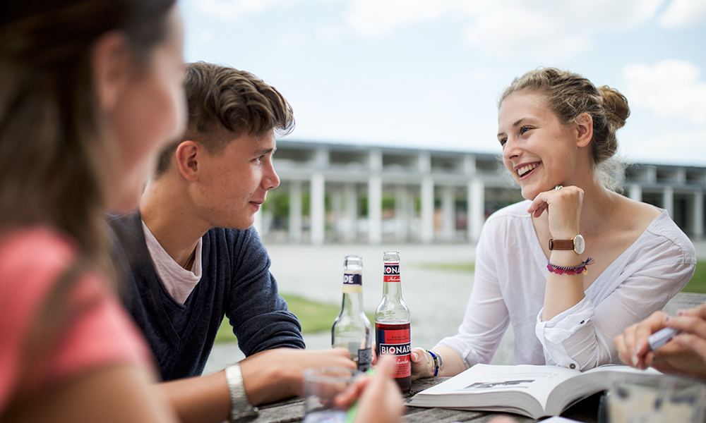 Drei Kollegiaten sitzen am Campus Härlen zusammen an einem Tisch mit Getränken und lachen