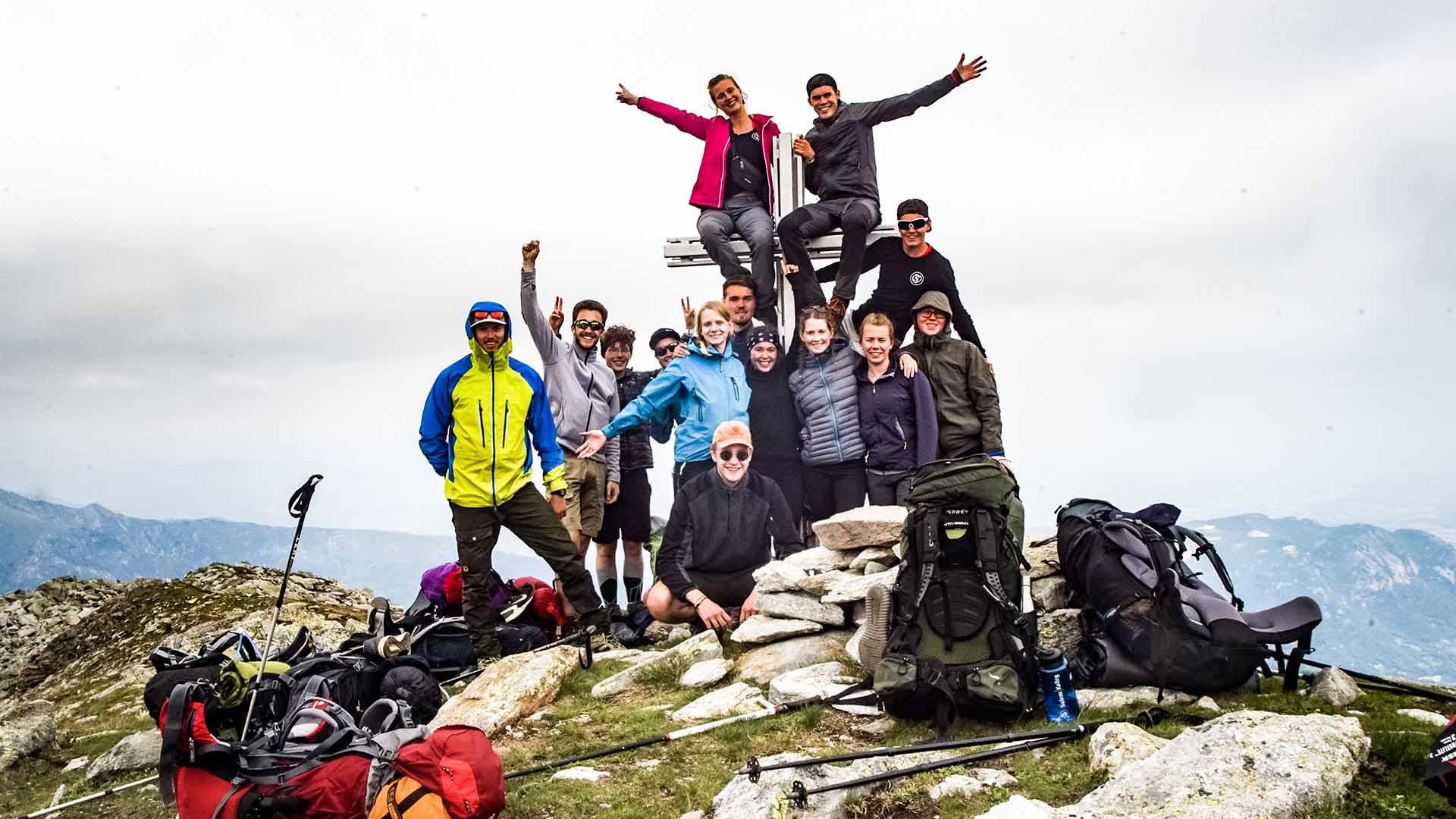 Eine Outdoor-Gruppe posiert auf dem Gipfel eines Berges mit Berglandschaft im Hintergrund