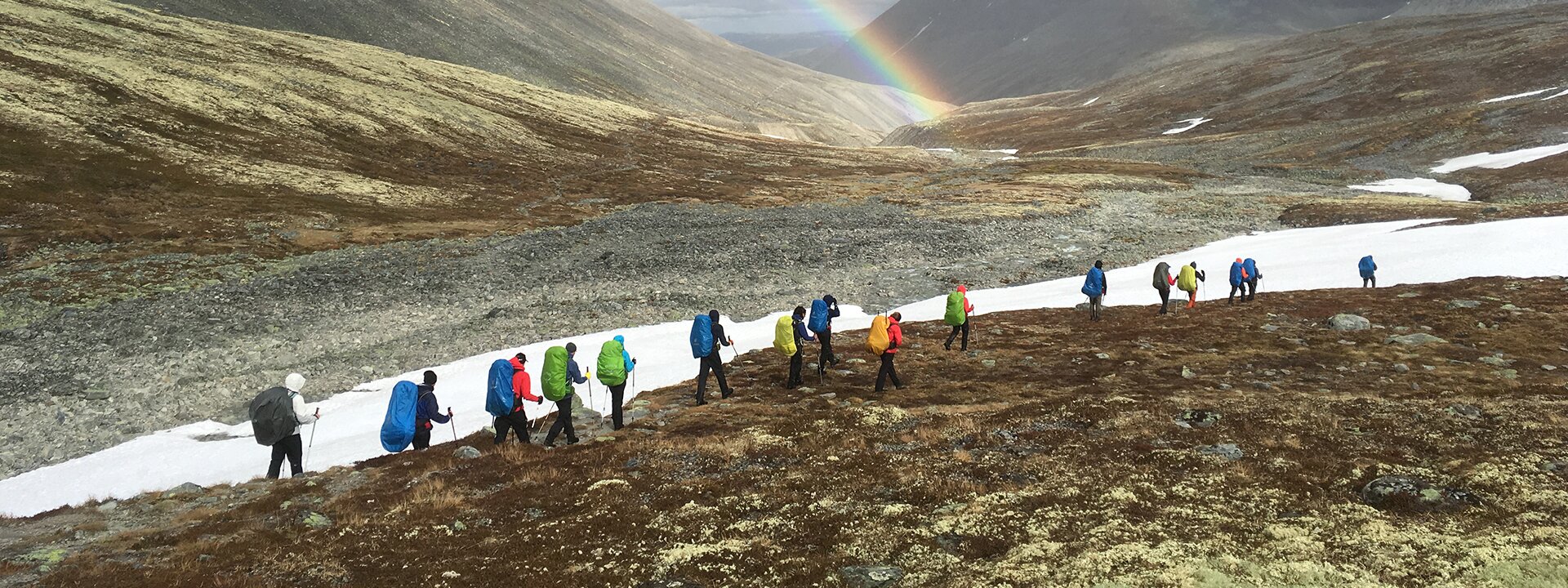 Eine Outdoor Gruppe in einer Berglandschaft in Norwegen mit Regenbogen im Hintergrund. Outdoor Education in alpinem Gelände.